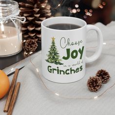 a white coffee mug sitting on top of a table next to an orange and pine cone