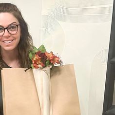 a woman holding two brown paper bags with flowers in them and smiling at the camera