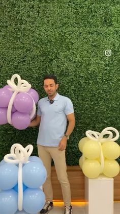 a man standing next to balloons in front of a wall with greenery behind him