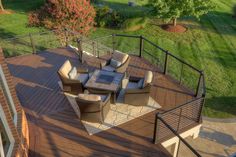 a deck with chairs and tables on it in the middle of a grassy area next to trees