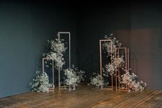 an arrangement of white flowers on a wooden floor in front of a blue wall with gold frames