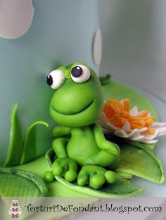 a green frog sitting on top of a leaf next to a white plate with an orange flower