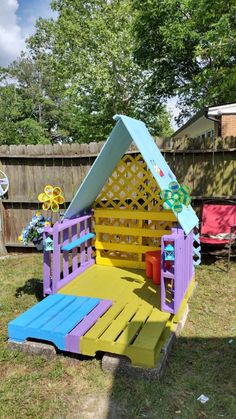 a small wooden house made out of pallets in the yard with colorful paint on it