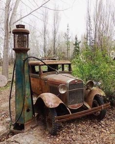 an old rusted out car sitting in the woods next to a light pole and lamp post