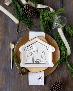 a plate with a nativity scene on it next to pine cones and napkins