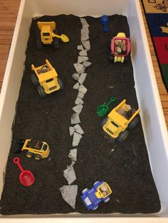 toy cars and construction vehicles are on the road made out of black sand in a bathtub