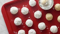 there are many snowball cookies on the red tray with a small bowl of powdered sugar