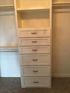 an empty closet with white drawers and shelves on the wall next to carpeted floor