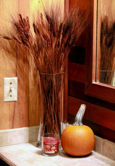 there is a vase with dried grass in it next to a pumpkin on the counter