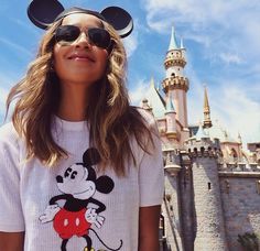 a woman standing in front of a castle with mickey mouse on her t - shirt