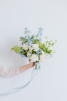 a woman holding a bouquet of white and blue flowers in her hand with a ribbon around it