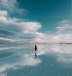 a person standing in the middle of a large body of water under a cloudy blue sky