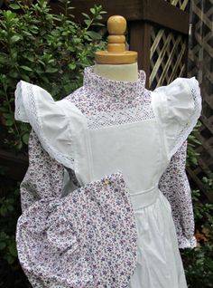 a white dress with flowers on it and a wooden mannequin in the background