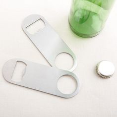 two bottle openers sitting on top of a table next to a green cup with a button