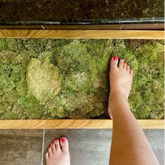 a woman's feet with red nail polish standing in front of a moss floor