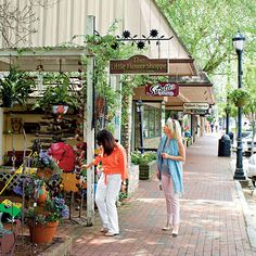 two women walking down the sidewalk in front of a store with lots of potted plants