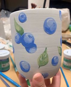 a hand holding up a cup with blueberries painted on it