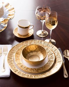 a wooden table topped with gold plates and silverware