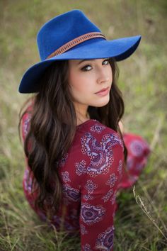 a woman wearing a blue hat laying on the ground with her hands in her pockets