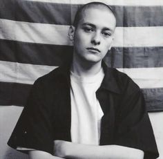 black and white photograph of a man with arms crossed in front of an american flag