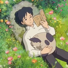 a man sitting in the grass reading a book with a cat on his lap next to him