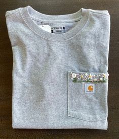 Everyone loves a Carhartt Tshirt, especially when they are extra special! These tshirts are hand embroidered with florals by a local artist in Pine Plains and made to order. Each tshirt is unique, so colors and shapes may vary (flower colors will change to match each tshirt color). Special requests can be made by contacting the store. Loose Fit Heavyweight Short-Sleeve Pocket T-shirt Color: Heather Gray Casual Crew Neck T-shirt With Floral Applique, Casual Cotton T-shirt With Embroidered Patch, Casual T-shirt With Embroidered Patch And Crew Neck, Casual Crew Neck T-shirt With Embroidered Patch, Casual T-shirt With Embroidered Patch, Casual T-shirt With Custom Embroidery For Everyday, Casual Everyday T-shirt With Custom Embroidery, Casual Tops With Embroidered Patch For Spring, Casual Cotton T-shirt With Floral Applique