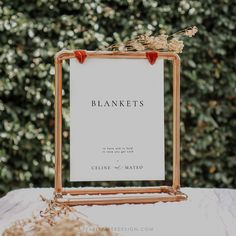 a white sign sitting on top of a table next to a plant filled with flowers