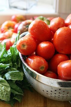 a metal colander filled with lots of tomatoes and lettuce on top of a wooden table