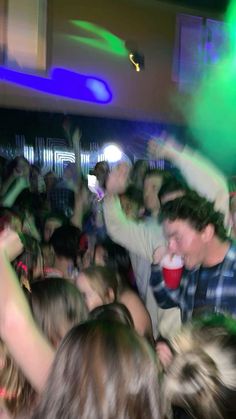 a large group of people are dancing at a party with green and blue lights on the ceiling