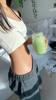 a woman holding a green smoothie in her right hand and showing off her stomach