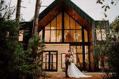 a bride and groom standing in front of a large wooden building with tall trees around them