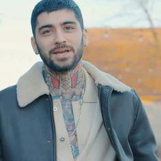 a man with blue hair wearing a leather jacket and tattoos on his face is looking at the camera