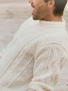 a man in a white sweater is holding a frisbee on the beach with his mouth open