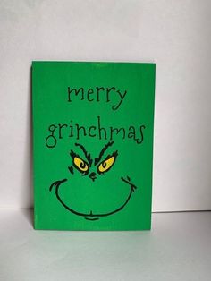 a green christmas card with the words merry grinmas on it's face and yellow eyes