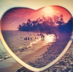 a heart - shaped frame with people swimming in the ocean at sunset on a beach