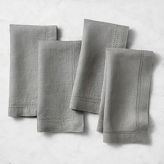 three linen napkins with stitching on the edges, one in grey and one in white