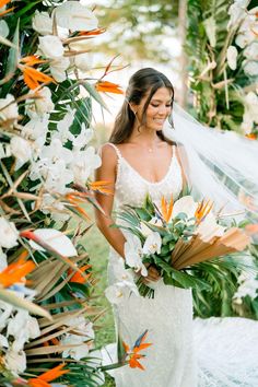 a woman in a wedding dress holding a bouquet and standing under an arch with flowers