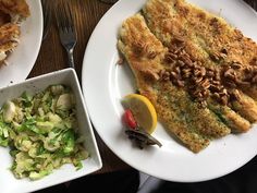 two white plates with food on them sitting on a table next to a bowl of salad