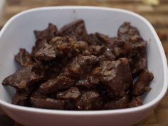 a white bowl filled with meat on top of a wooden table