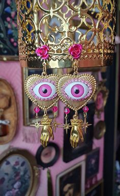 pink eye earrings hanging from a gold chandelier with pictures on the wall behind them