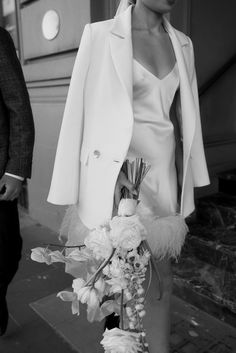 a woman in a white dress and jacket holding a bouquet