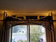 a model train set on top of a rail road bridge over a window in a house