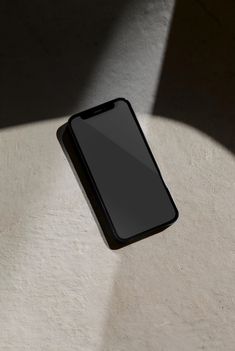 a black cell phone sitting on top of a white table next to a shadow cast wall