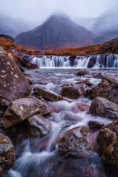 a mountain stream running between large rocks and boulders in the foreground, with mountains in the background