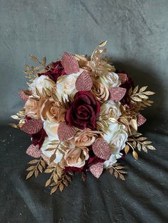 a bridal bouquet with red roses and gold leaves on a black tablecloth background