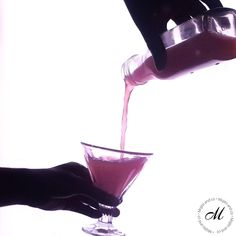 someone is pouring pink liquid into a glass in front of a white background with black hands