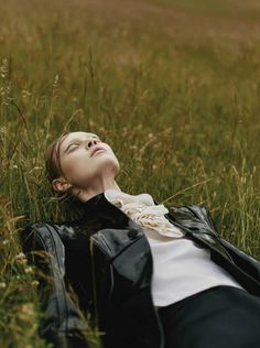 a woman laying in the grass with her eyes closed and looking up to the sky