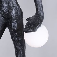 a black statue holding a white ball in it's right hand and its left arm