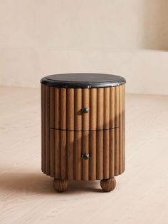 a round wooden box with black leather top on a wood floor in front of a white wall