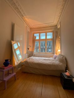 a bed sitting in a bedroom under a window next to a table with a vase on it